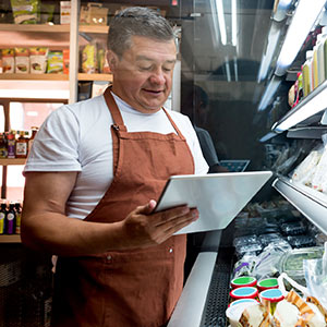 Man wearing apron using tablet to take inventory at grocery store.